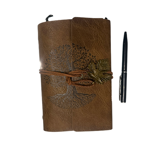 small leather journal with embossed tree design, wrap closure, and leaf charm on rustic background